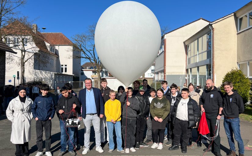 Der Ballon ist gefüllt. Gleich geht's ab in den Himmel: Fünfter von rechts: Thomas Mahlmann (zdi-Zentrum Lippe.MINT), von links: Marvin Rissiek und Robin Odasso (beide Stratoflights GmbH & Co. KG) mit den teilnehmenden Schülerinnen und Schülern. (Foto: Lippe Bildung eG)